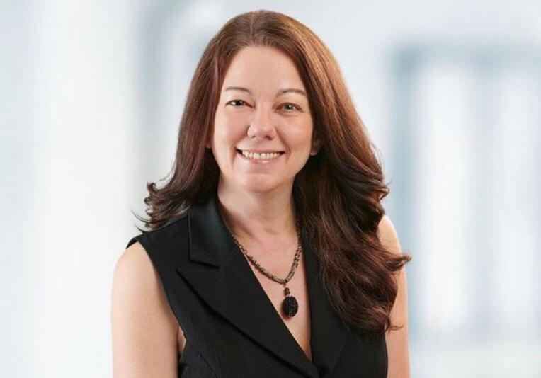 A smiling woman with long brown hair in a black sleeveless top.